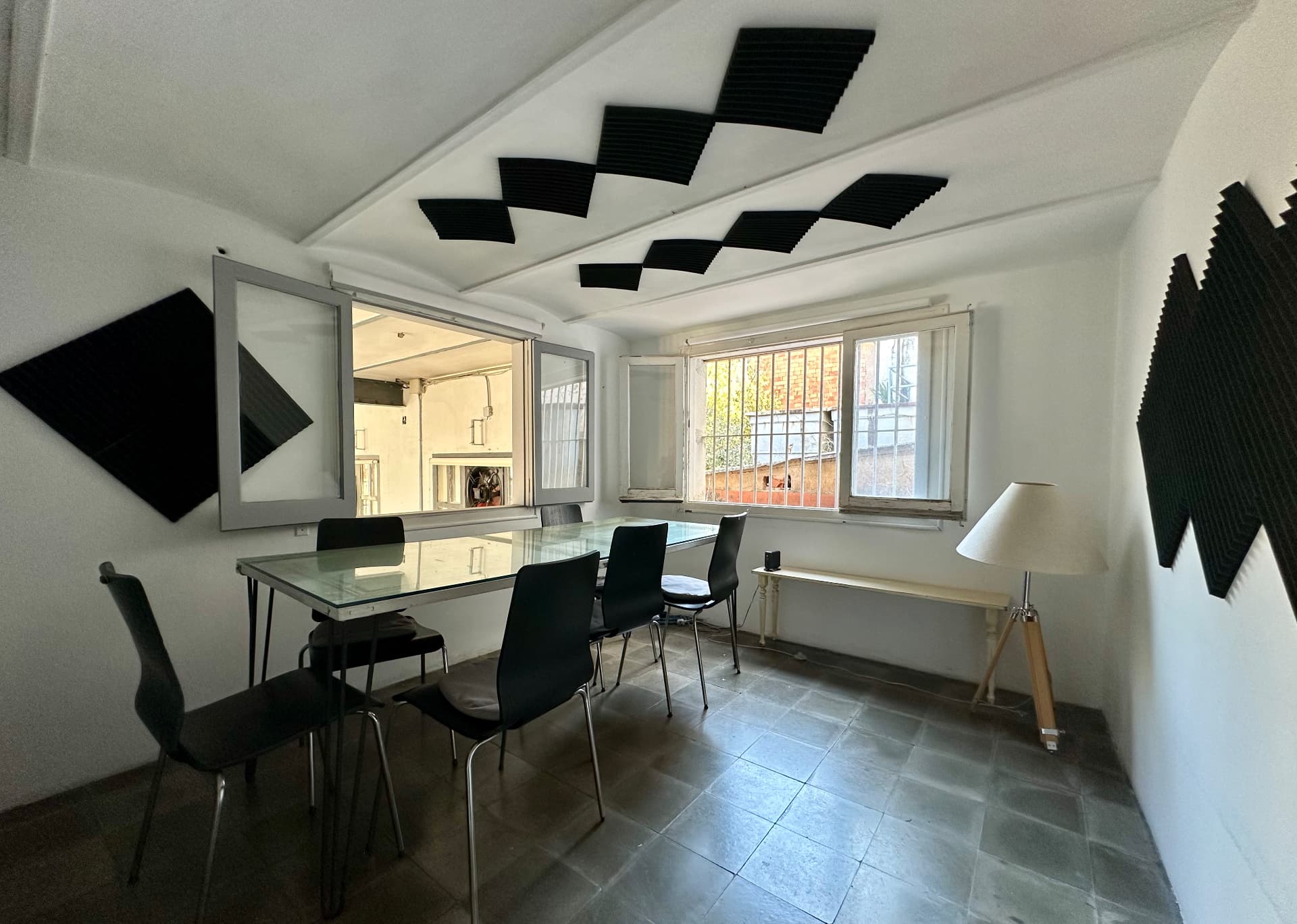 La sala de reuniones de La Fabriqueta, una mesa de cristal con sillas, paneles acusticos y ventanas al jardin