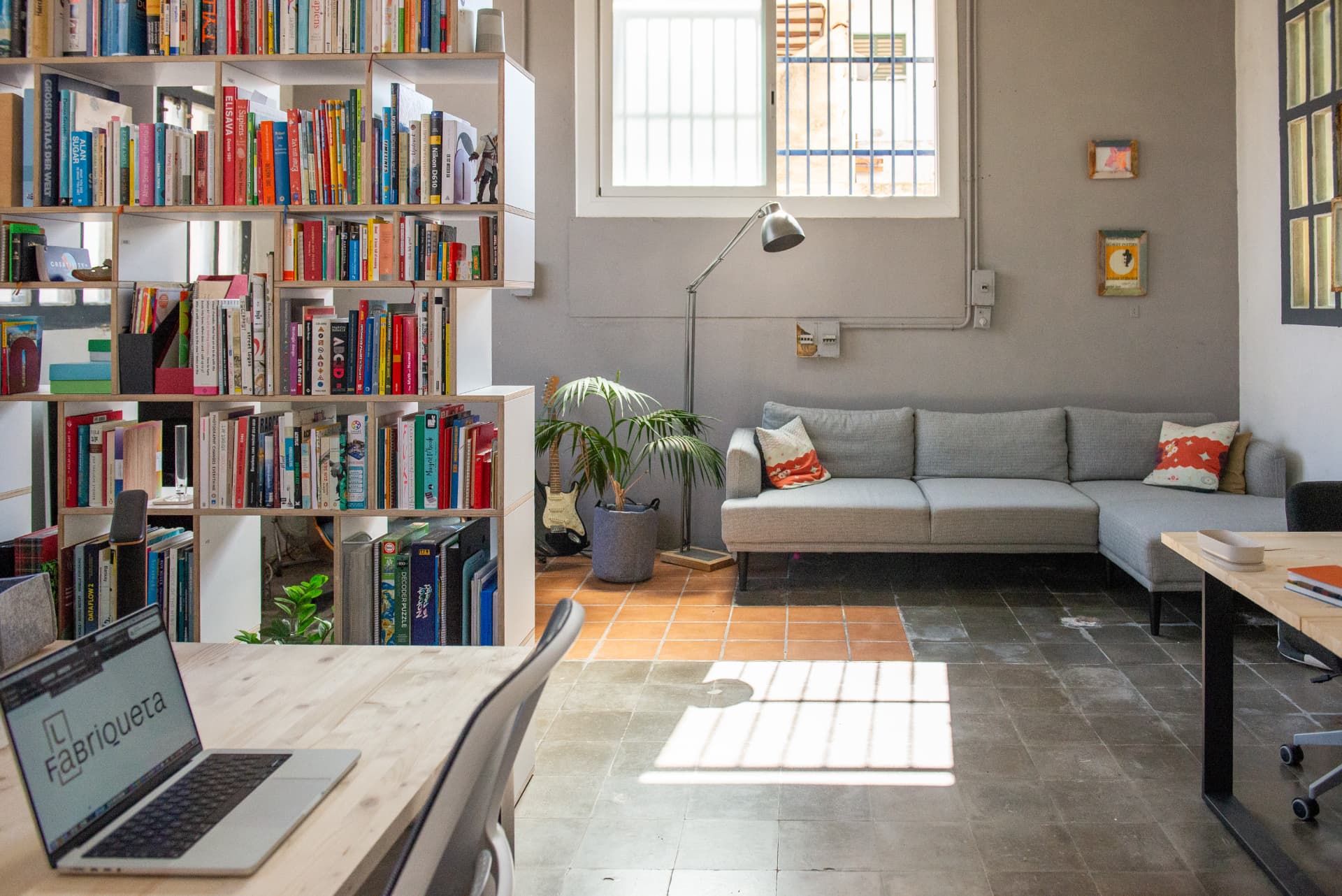 El rincón de lectura de La Nave: biblioteca compartida, sofá y un portátil con el logotipo de La Fabriqueta